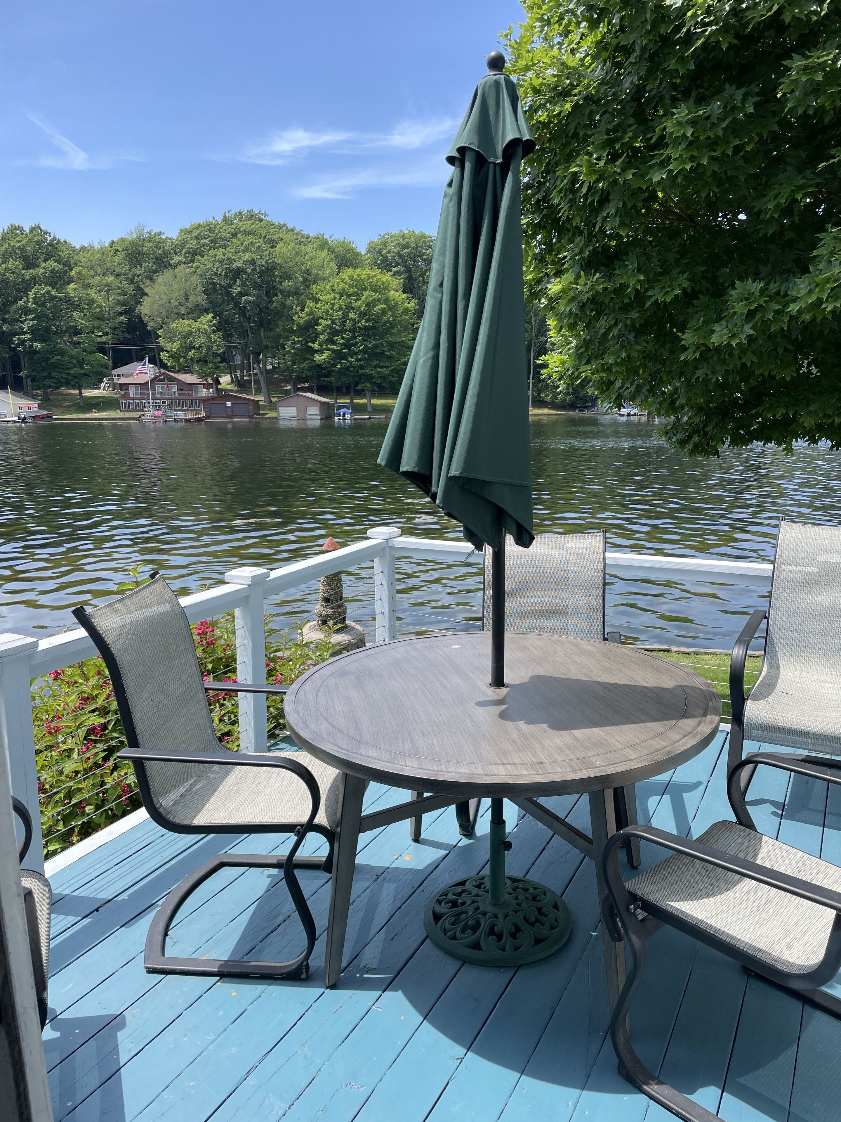 A deck with a round table and chairs, an umbrella, and a view of a lake with buildings in the background.