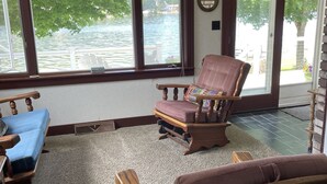 Un salon avec vue sur un lac, un canapé bleu, un fauteuil à bascule en bois et une table basse en bois sur laquelle se trouve une boîte à mouchoirs.