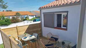 Eine kleine Terrasse mit Tisch und zwei Korbstühlen, einem kleinen Topfpflanzen und einem Fenster mit Rollläden.