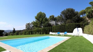 Ein rechteckiger Swimmingpool mit weißem Deckrand, umgeben von gepflegtem Rasen und einem weißen Zaun.