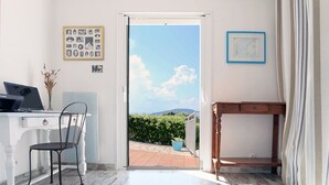 Ein Zimmer mit Schreibtisch, Stuhl und Blick auf einen Garten durch eine offene Tür.