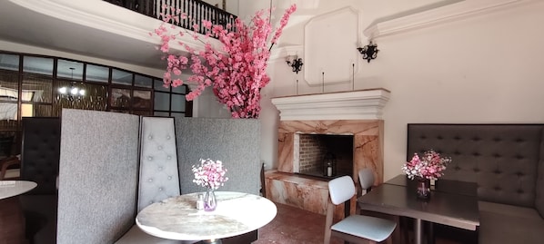A dining area with round tables, cushioned seating, a fireplace, and decorative flowers.