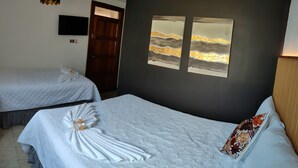 A hotel room with two beds, each with a neatly arranged towel and a decorative pillow. There are wall-mounted artwork and a television above the beds.