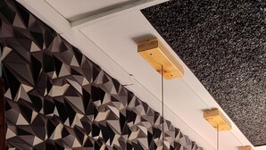 A bar area with a geometric patterned wall, wooden bar counter, and black stools.