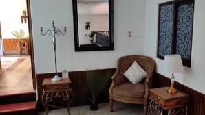 A room with a wooden chair, a small table with a lamp, a potted plant, and a mirror on the wall.