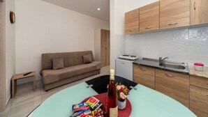 Un espacio habitable compacto con kitchenette, un sofá y una mesa de comedor con una botella y aperitivos.