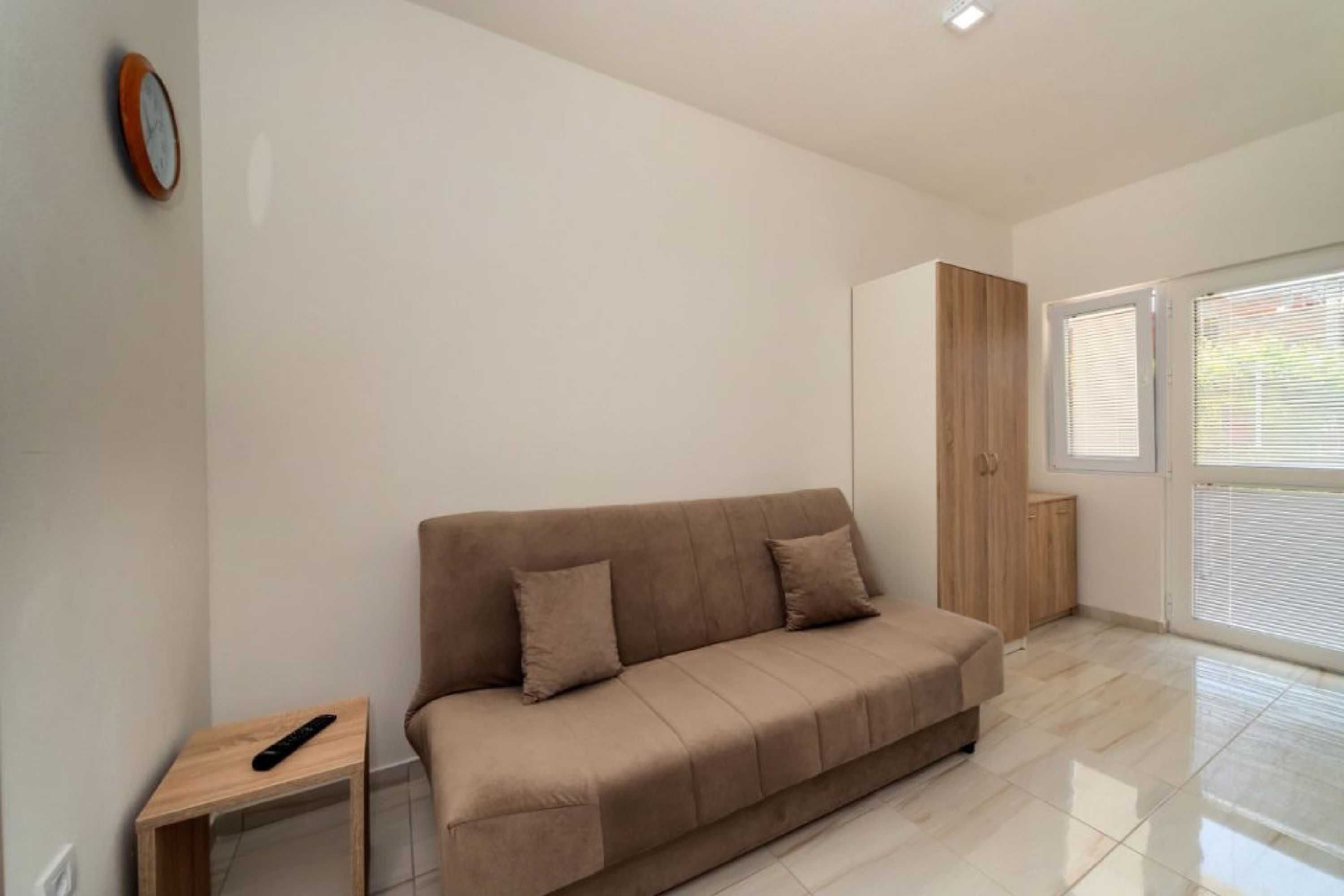 Una sala moderna con un sofá color beige, una pequeña mesita de madera y un ventanal con persianas.