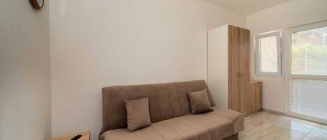 Una sala moderna con un sofá color beige, una pequeña mesita de madera y un ventanal con persianas.