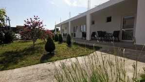 Un edificio moderno con un área de estar exterior cubierta, un césped cuidado y un automóvil estacionado.
