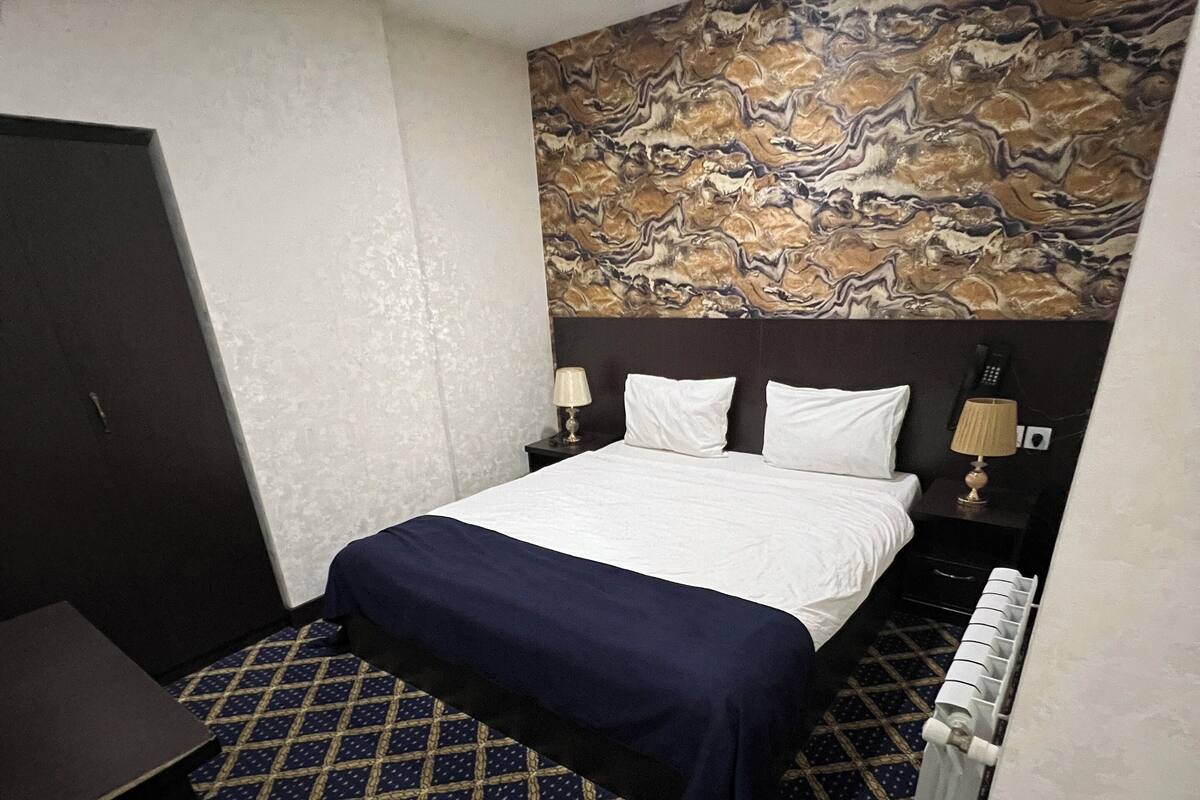 Une chambre d’hôtel avec un lit, un bureau, une chaise, une moquette à motifs et un sol en marbre.