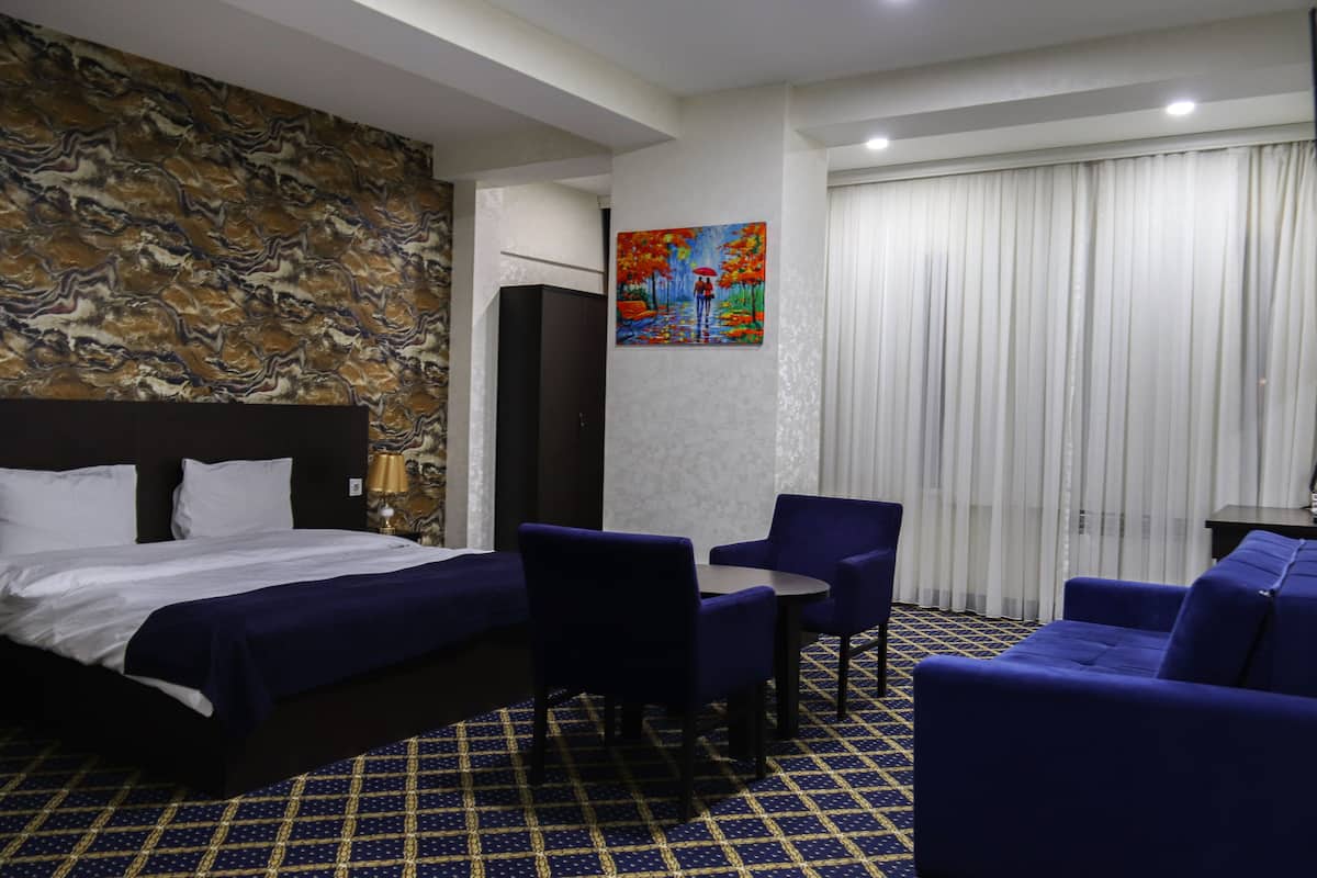 Une chambre d’hôtel avec un lit, un bureau, deux chaises, un tableau au mur et une moquette à motifs.