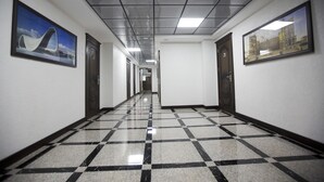 A hallway with a checkered floor, framed pictures on the walls, and doors on both sides.