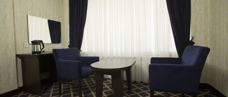 Une chambre d’hôtel équipée d’un bureau, de deux chaises, d’une petite table, d’un miroir et d’une fenêtre avec des rideaux.