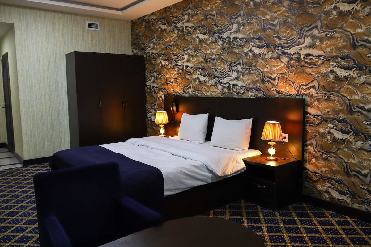 Une chambre d’hôtel avec un grand lit, deux lampes de chevet, une armoire et un mur décoré d’un motif.