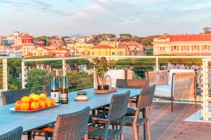 A terrace with a table set for dining, featuring wicker chairs, a bottle of wine, and a potted plant. - Experience Rome’s grandeur from our Skylife Penthouse with 360° views of Tiber (Roma)