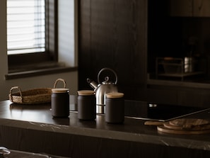 A kitchen counter with a kettle, two mugs, and a woven basket.