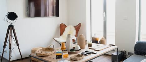 Una sala de estar moderna con un televisor de pantalla plana grande montado en la pared, un trípode, un sillón de cuero, un sofá y una mesa de centro con varios objetos encima.