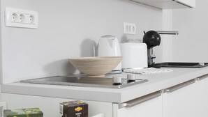 Een moderne keuken met een wit aanrecht, een koffiezetapparaat, een waterkoker, een kom en een koffiemachine.