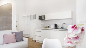 Een moderne, minimalistische woonkamer met een witte bank, een salontafel en een keukenhoek met witte kasten en een magnetron.