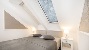 Een slaapkamer met dakraam, een bed met grijze beddengoed, nachtkastjes met lampen, en een houten vloer.