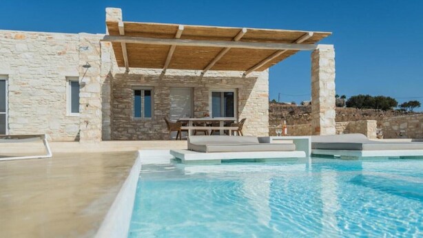 Una villa de piedra con piscina, mobiliario de exterior y una pérgola.