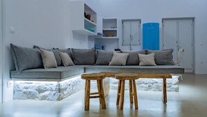 Una sala de estar moderna con un área de asientos integrada tipo banca, taburetes de madera y una cocina con armarios y un refrigerador azul.