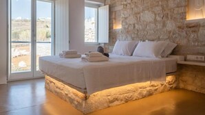 Un dormitorio con pared de piedra, una cama con ropa blanca y vistas amplias a través de puertas de vidrio.