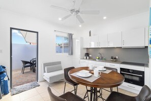 A modern kitchen with white cabinets, a dining table with chairs, and a ceiling fan.