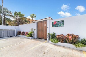 Un espace de stationnement clos, avec un mur blanc, une porte en bois et des plantes en pot.