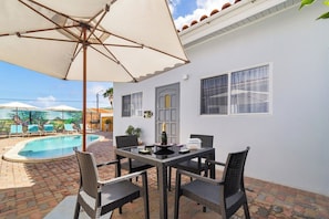 An outdoor patio with a pool, a table with chairs, and a large umbrella.