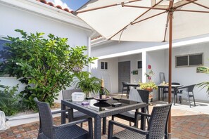 An outdoor patio area with a table and chairs, a large umbrella, and potted plants. - Prime Aruba Location: 2BR Apartment near Beaches (Noord)
