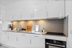 A modern kitchen with white cabinets, a built-in oven, and a coffee maker.