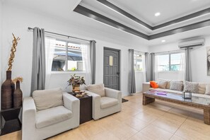 A modern living room with a sofa, armchairs, a coffee table, and a door. - Prime Aruba Location: 2BR Apartment near Beaches (Noord)