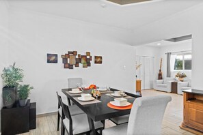 Ein Essbereich mit einem schwarzen Tisch, gedeckt für vier Personen, umgeben von grauen Stühlen. Über dem Tisch befinden sich dekorative Wandelemente und links steht ein Blumentopf.