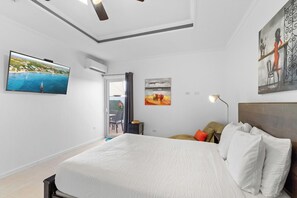 Ein Hotelzimmer mit einem Bett, einem an der Wand befestigten Fernseher, einem Gemälde und einem Fenster.