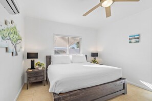 A bedroom with a bed, nightstands, a ceiling fan, a window, and wall art. - Prime Aruba Location: 2BR Apartment near Beaches (Noord)