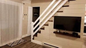 Ein modernes Wohnzimmer mit Treppe, einem an der Wand montierten Flachbildfernseher und einem gemusterten Teppich.