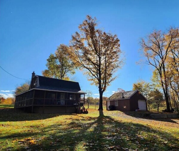 Ein zweistöckiges Haus mit einem großen Baum davor, umgeben von Herbstlaub.