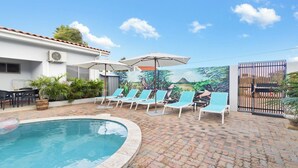 A swimming pool area with lounge chairs and umbrellas. - Family-Friendly 1BR Retreat w/ Pool & Beach Access (Noord)