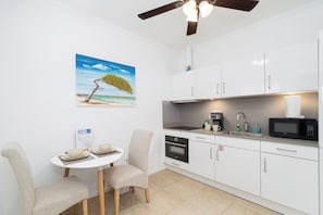 A compact kitchen with white cabinets, a microwave, a sink, and a ceiling fan. - Family-Friendly 1BR w/ Shared Pool, Noord (Noord)