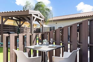 Un espace extérieur aménagé en terrasse, avec une table pour deux, une pergola et une vue sur un immeuble d’habitation en arrière-plan.