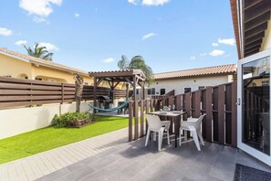A patio with a wooden pergola, a hammock, and a dining area with white chairs and a table.