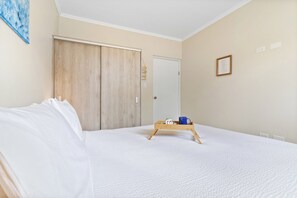 Une chambre à coucher avec un lit, une armoire en bois, une table de chevet avec un plateau, et un tableau encadré au mur.