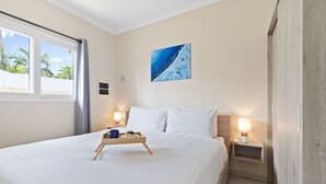 A neatly made bed with white linens, a bedside table with a lamp, and a window with curtains. - Cozy one-bedroom apartment in Little Sea (Noord)