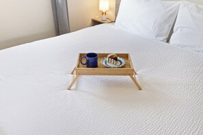 A neatly made bed with a tray holding a mug and a plate of food.