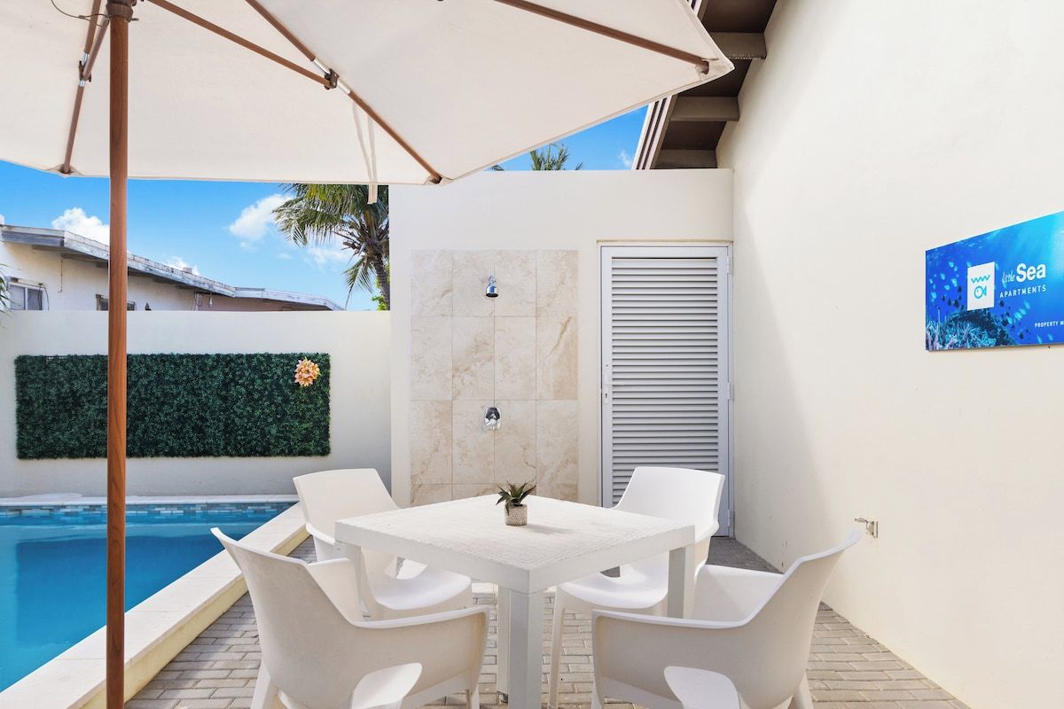 A poolside area with a white table and chairs, a small potted plant, and a wall-mounted air conditioning unit.