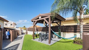 Un patio con una pérgola de madera, una mesa con sillas y una hamaca.