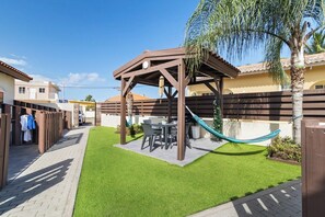 Una zona patio con una pergola in legno, un tavolo con sedie e un'amaca.