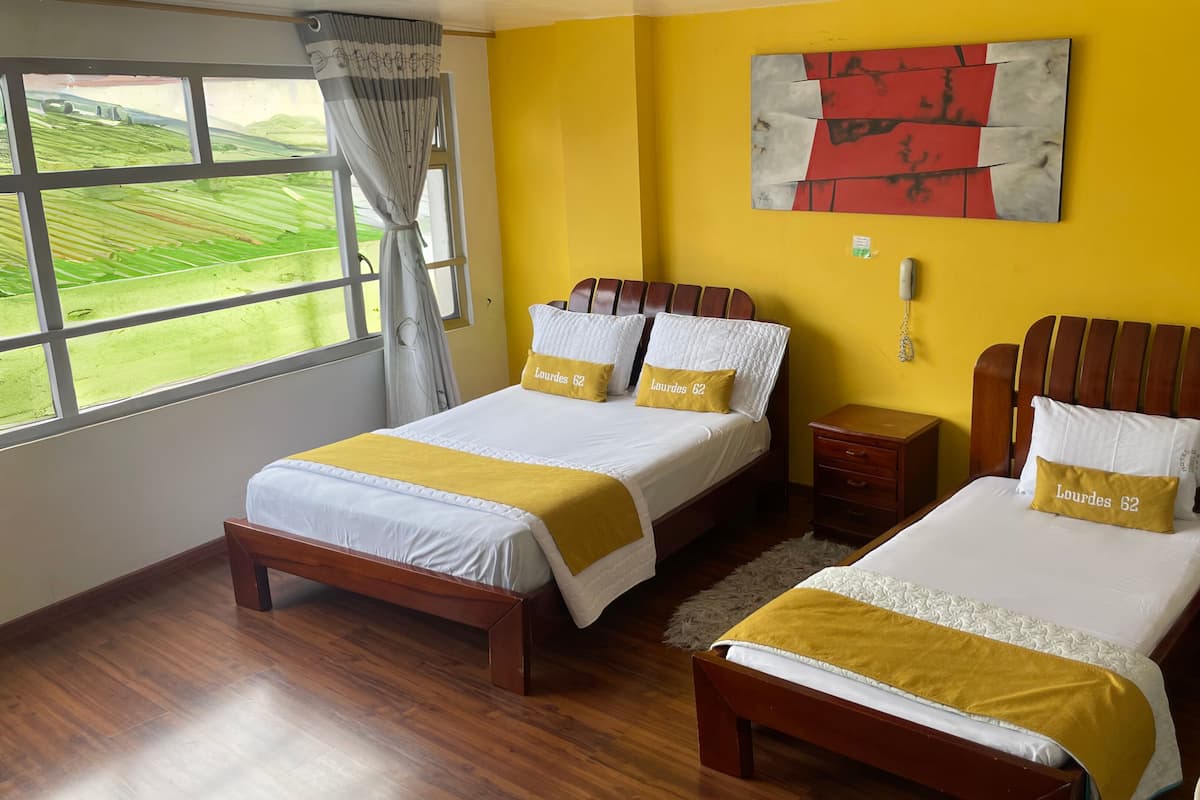 Habitación de hotel con dos camas, paredes amarillas y un ventanal con vistas a un paisaje verde.