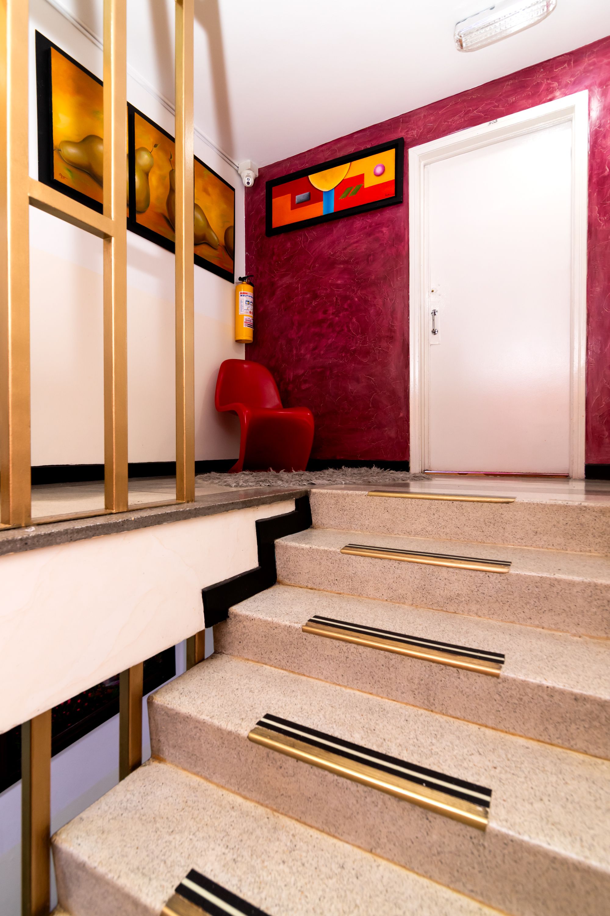 A staircase with beige steps and gold handrails, leading to a room with a red wall and a white door.